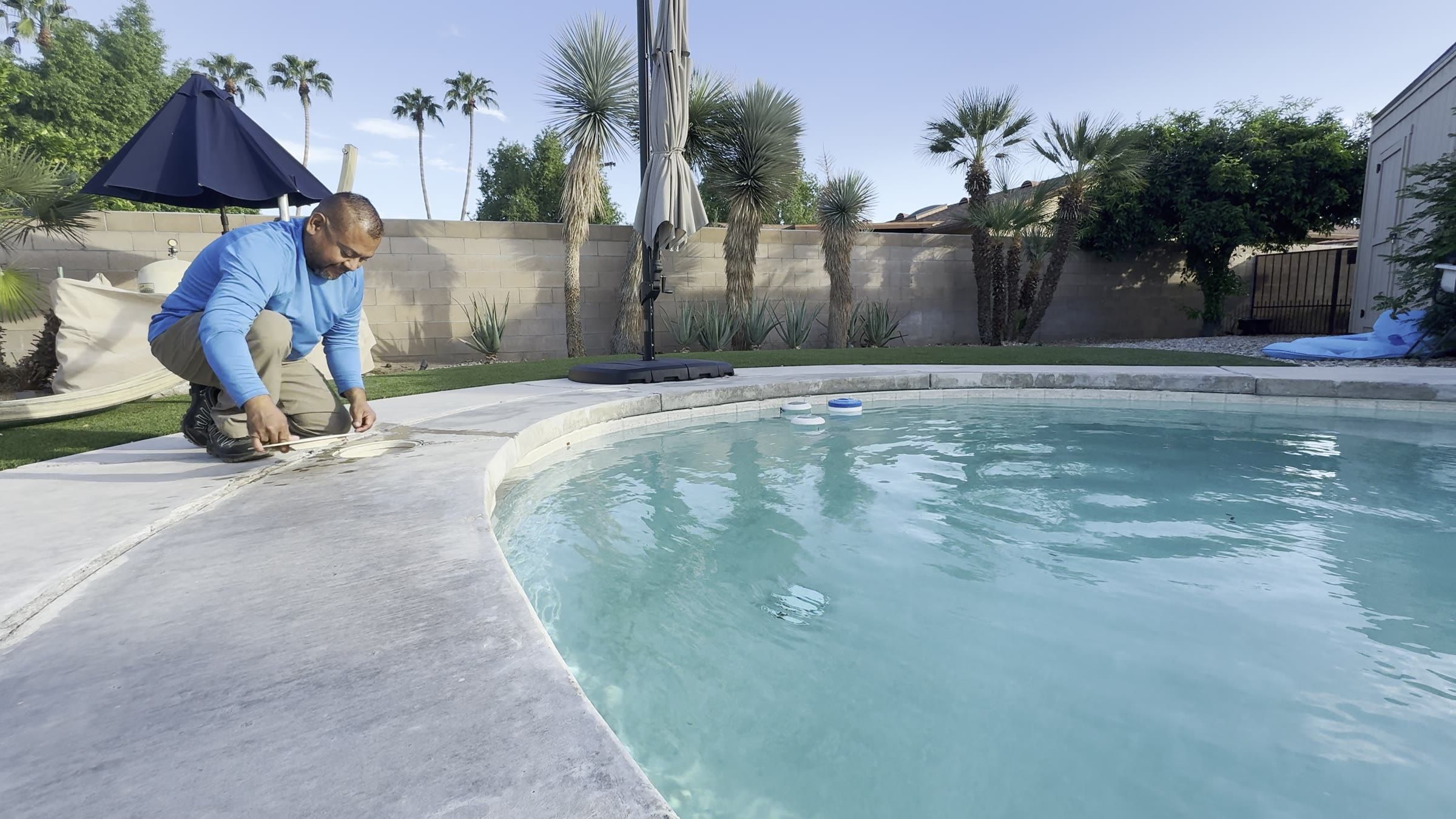 The owner cleaning a skimmer basket beside a backyard pool with palm trees