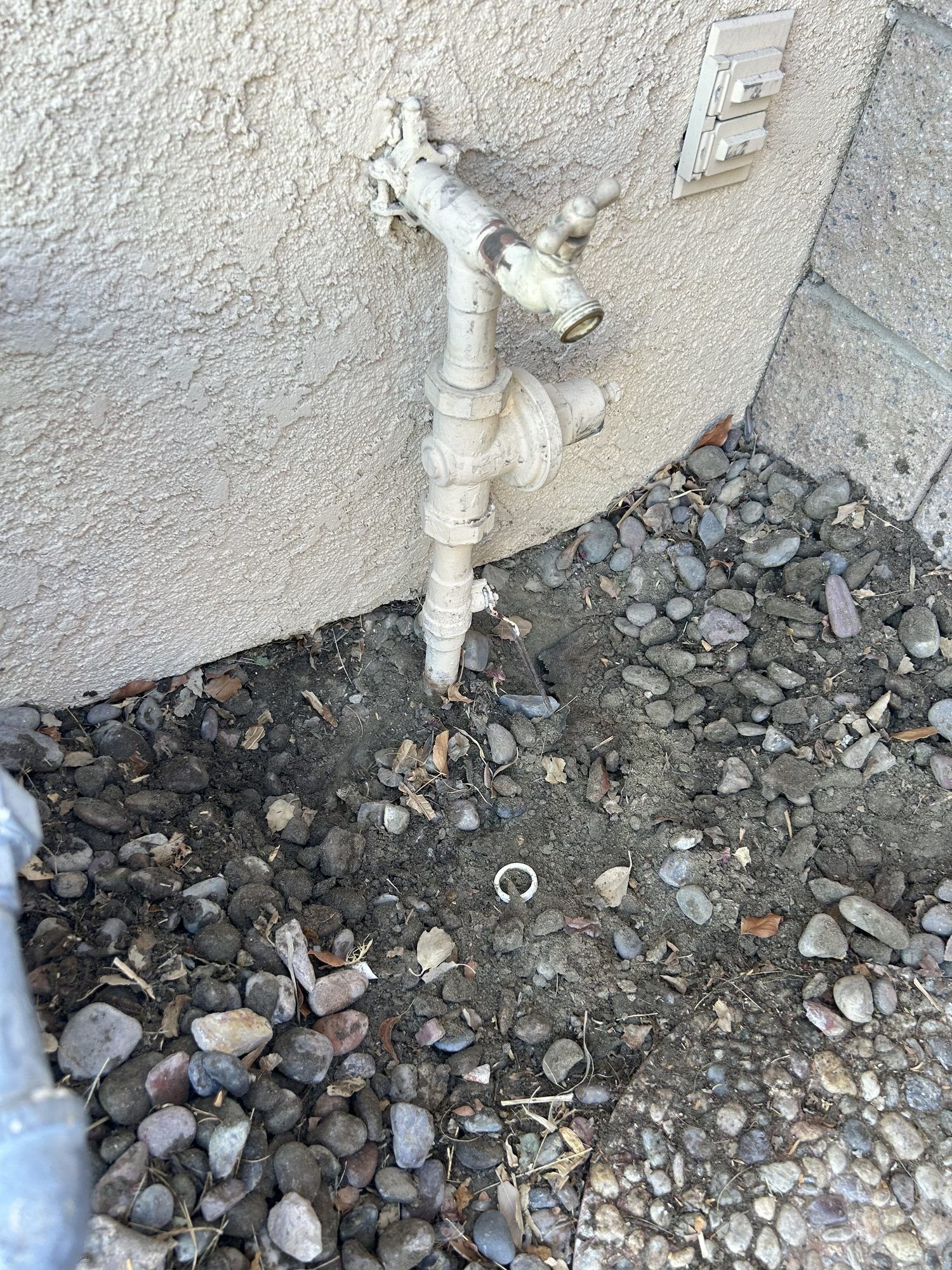 Old outdoor water valve with wet ground in the rock bed before the repair