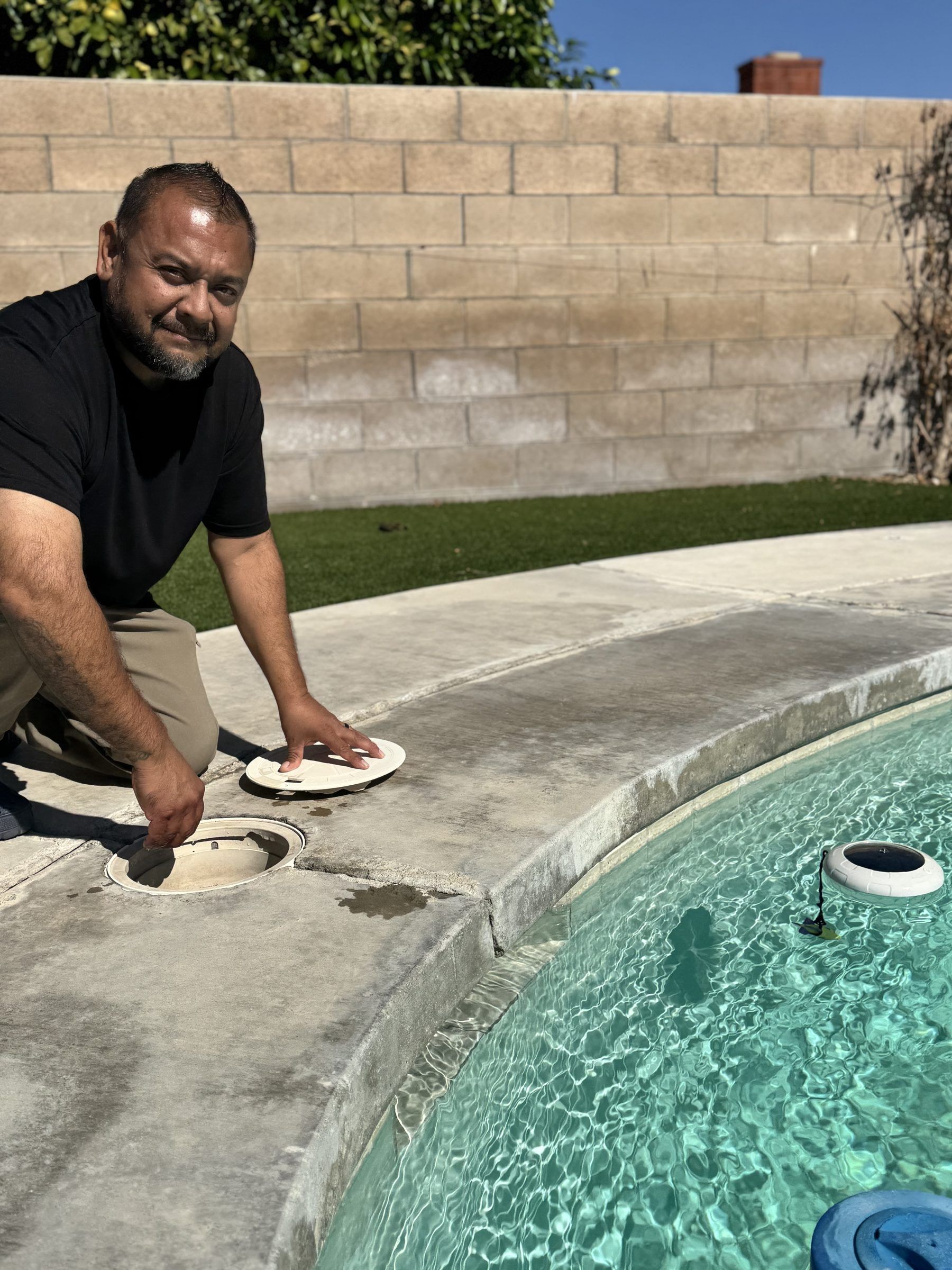 The owner kneeling at a pool skimmer, smiling at the camera